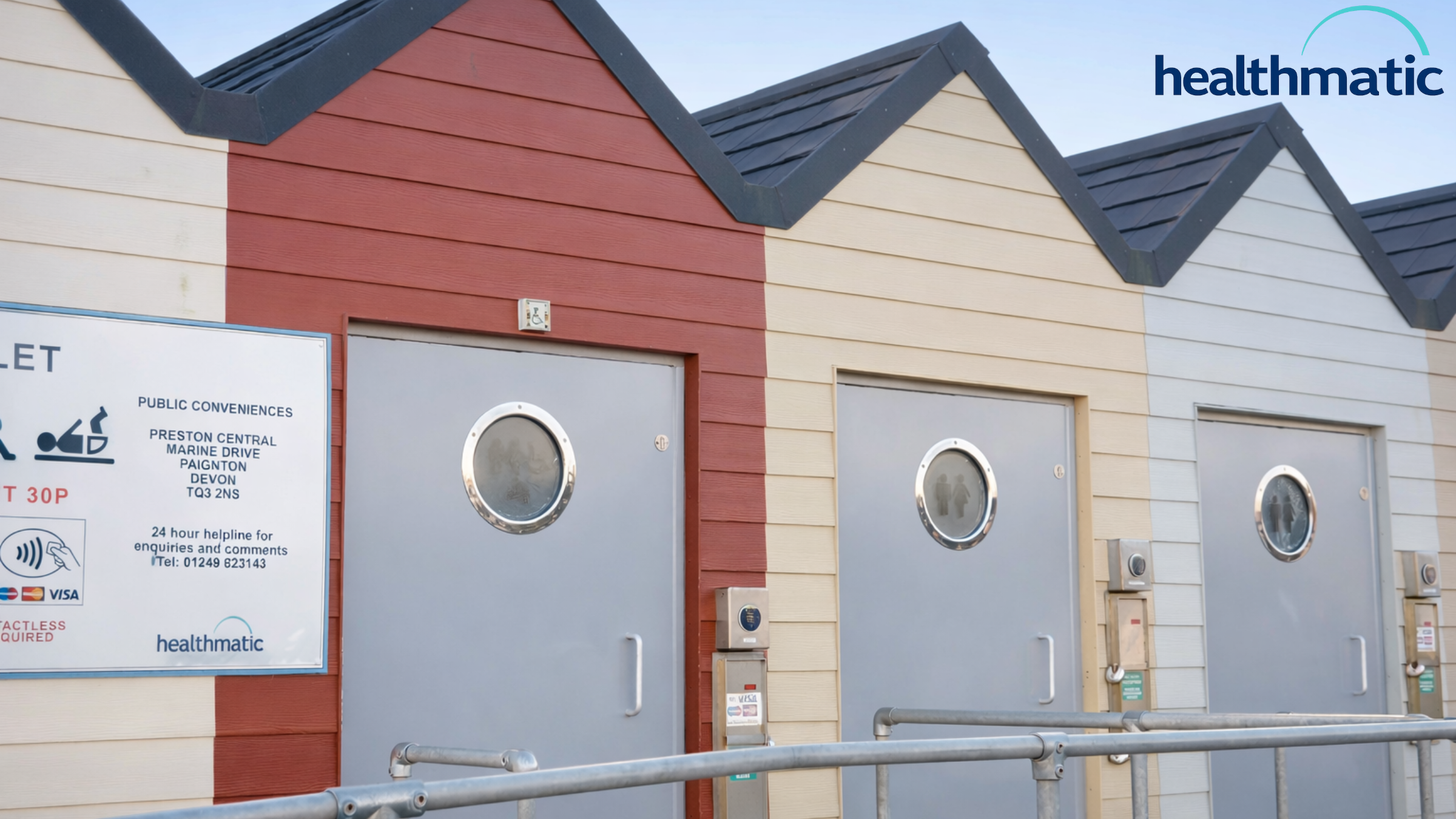 Row of seaside-style public toilet cubicles with grey doors and accessibility signage, at Preston Central, Marine Drive, Paignton, Devon.